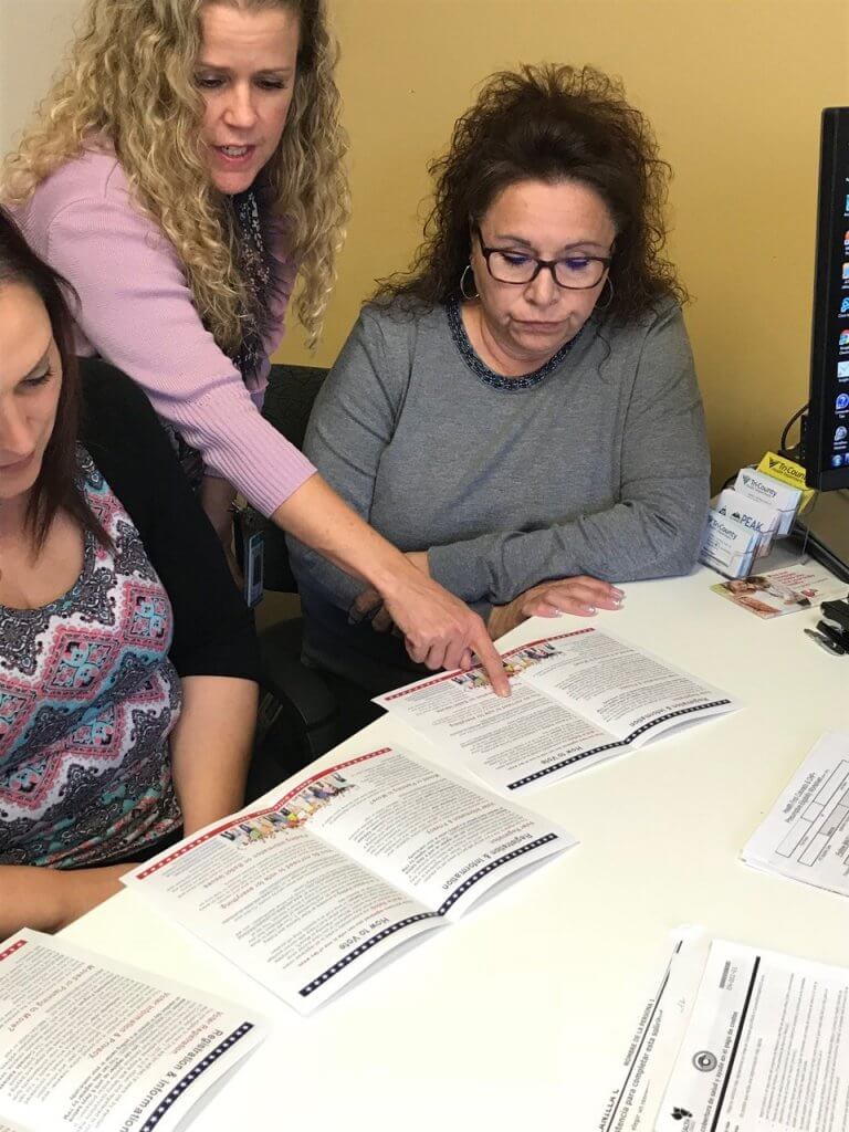 Three women review voter registration guide